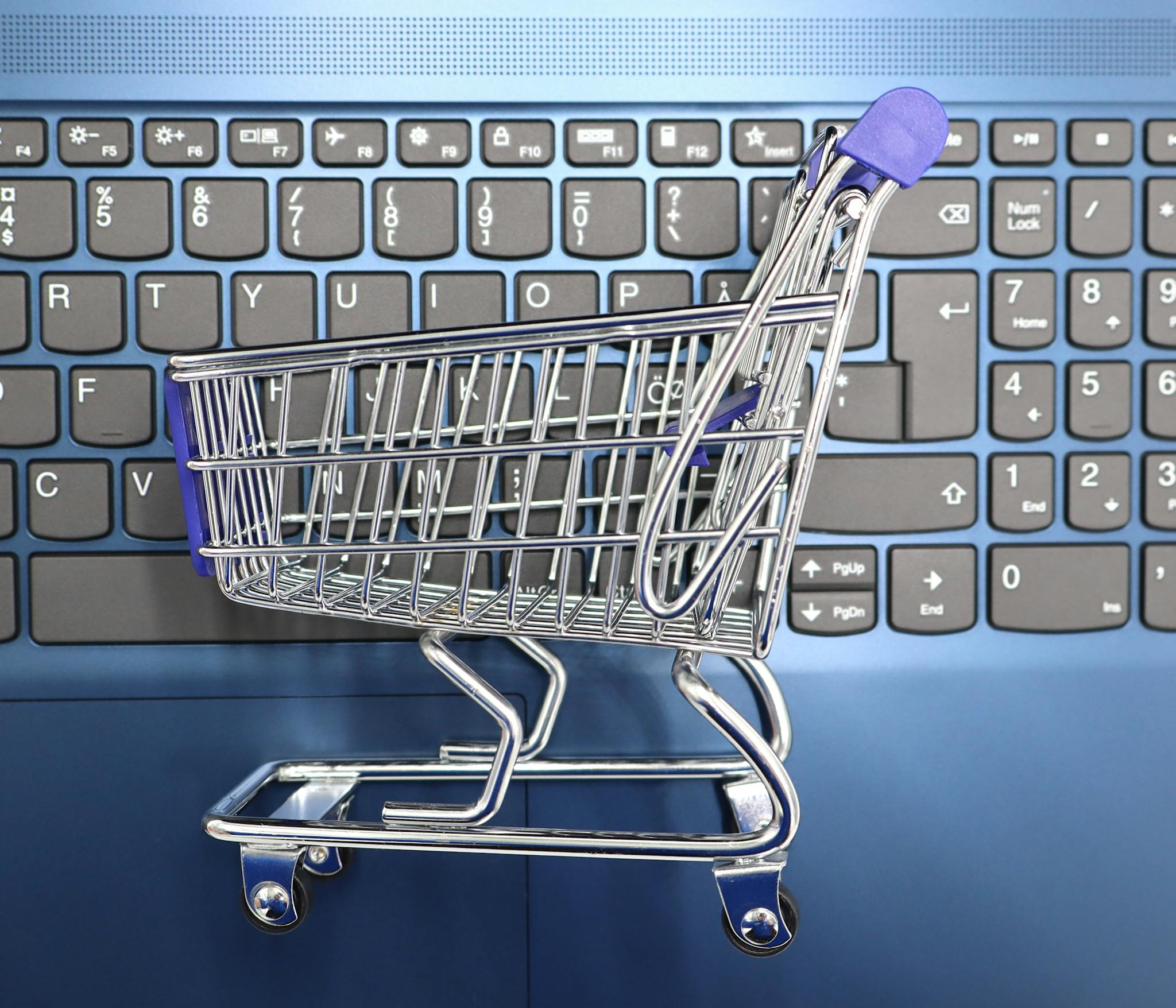 Home A miniature shopping cart placed on a laptop keyboard symbolizing online shopping and e-commerce.